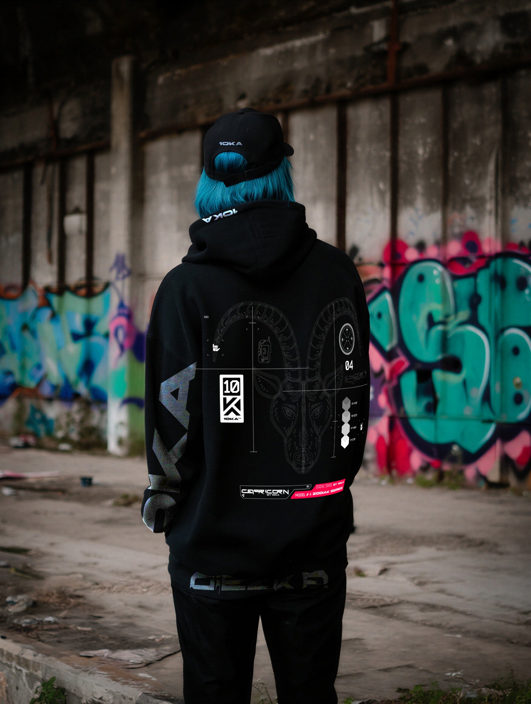 Model wearing the Zodiac Hoodie Capricorn by 10KA in an urban setting, back view, showcasing structured futuristic graphics inspired by ambition and authority.
