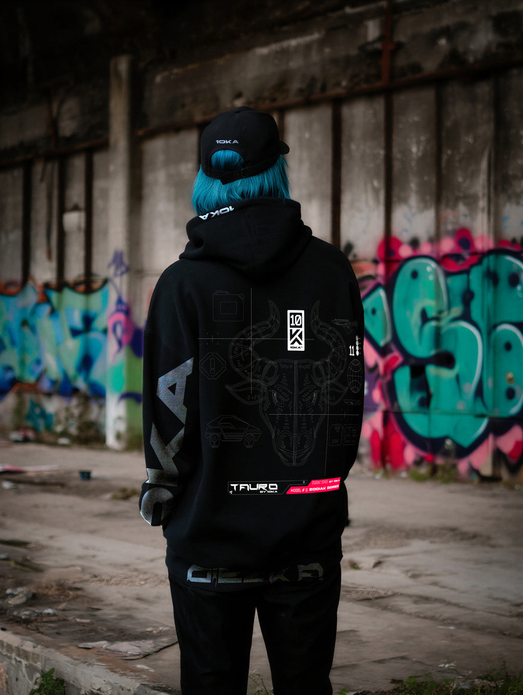Model wearing the Zodiac Hoodie Taurus by 10KA in an urban setting, back view, showcasing solid futuristic graphics inspired by endurance and grounded strength.
