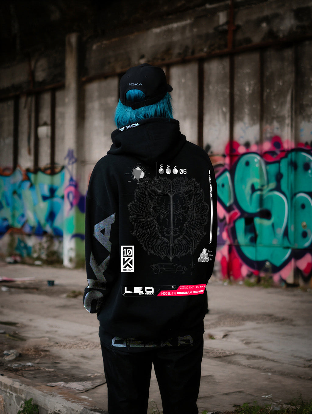 Model wearing the Zodiac Hoodie Leo by 10KA in an urban setting, unisex black hoodie with bold futuristic graphics, fire symbolism, and astrological Leo identity photographed from the back.