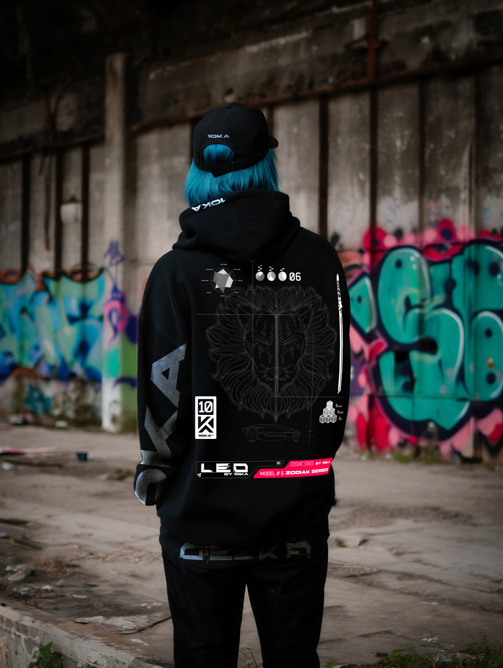 Model wearing the Zodiac Hoodie Leo by 10KA in an urban setting, unisex black hoodie with bold futuristic graphics, fire symbolism, and astrological Leo identity photographed from the back.